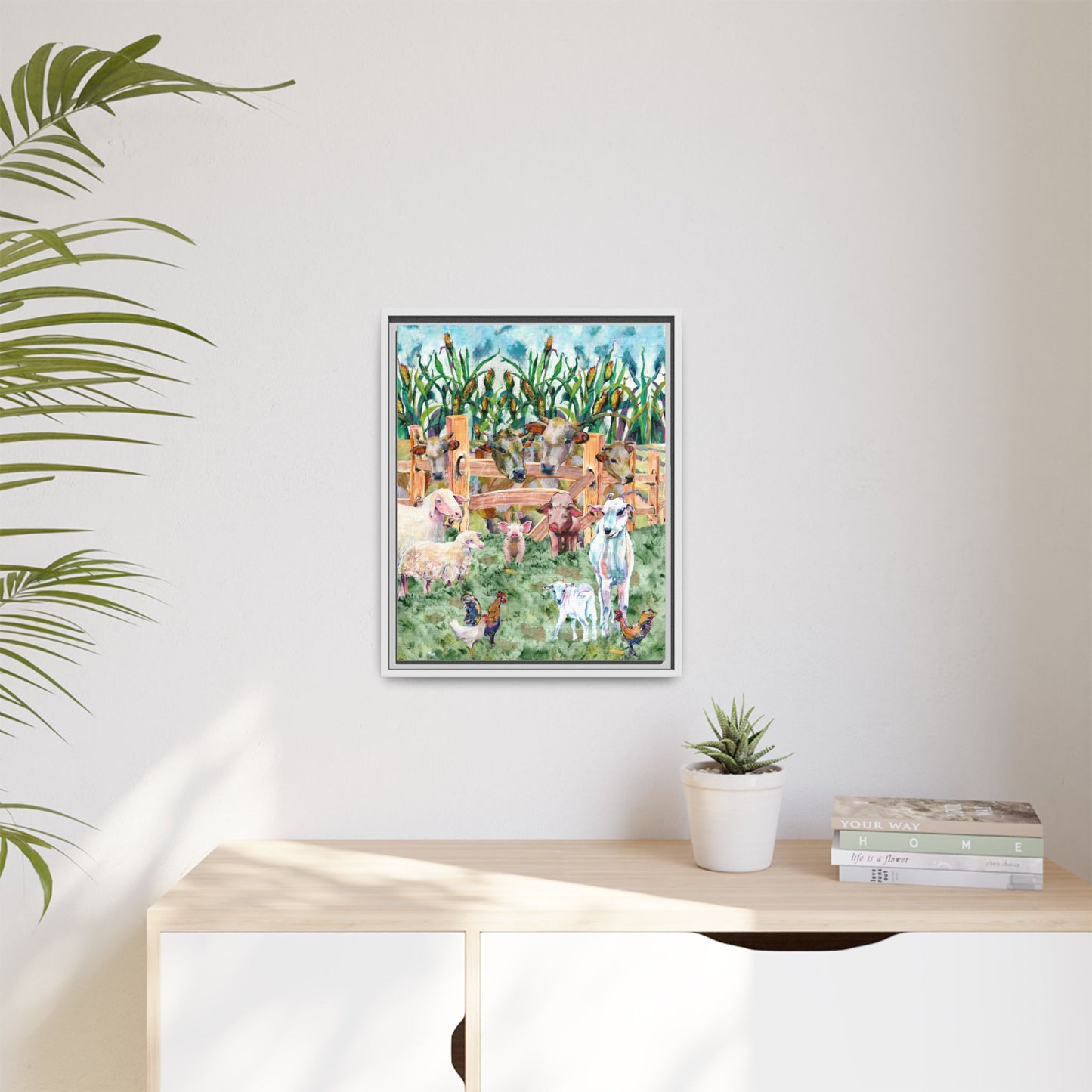 Framed artwork of animals in a field on a wall above a desk with plants and books.
