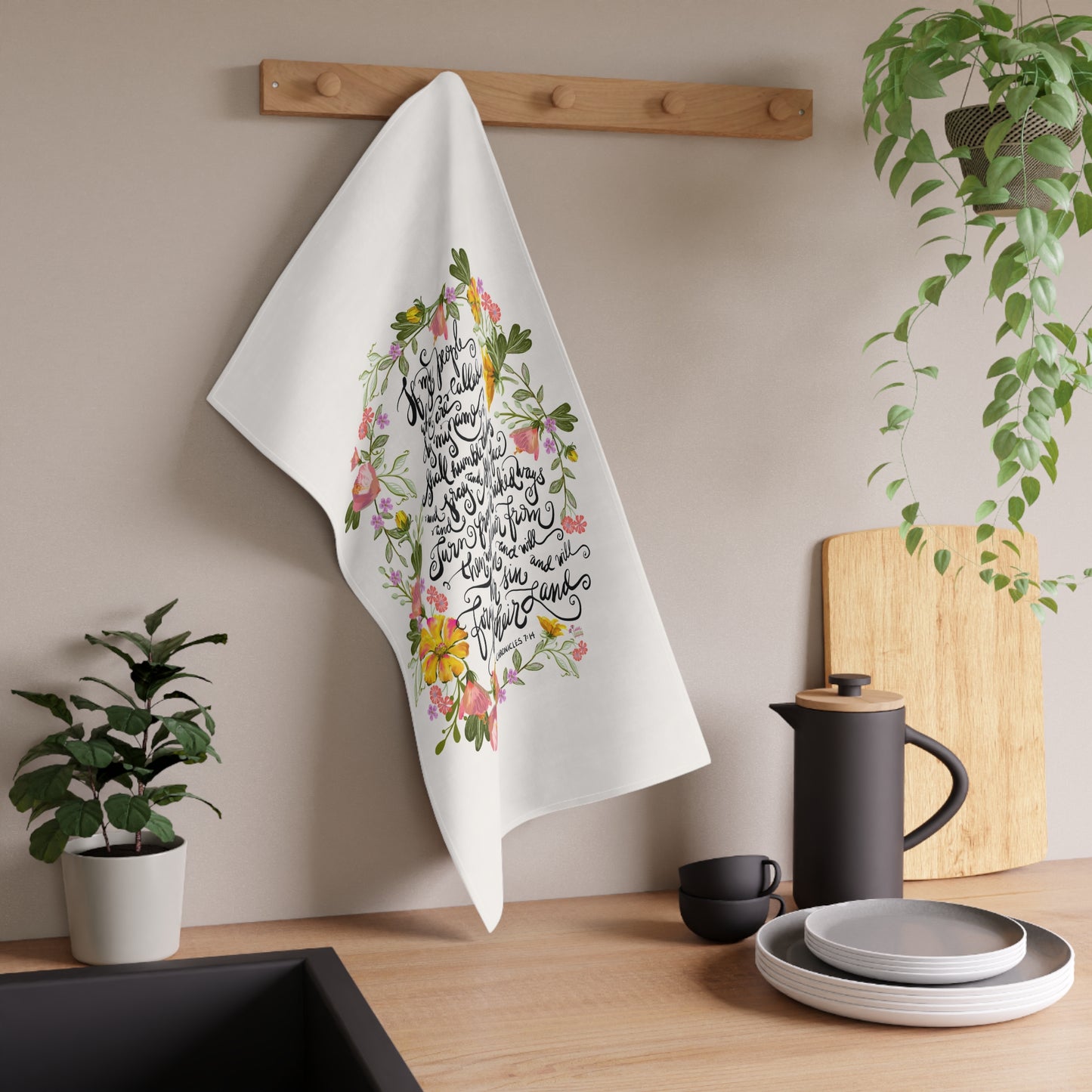 White towel with floral and Bible verse calligraphy design hanging on a wooden rack in a kitchen setting.