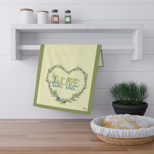 Decorative litchen towel with 'Love never fails' text on a kitchen shelf with a plant and bread basket.