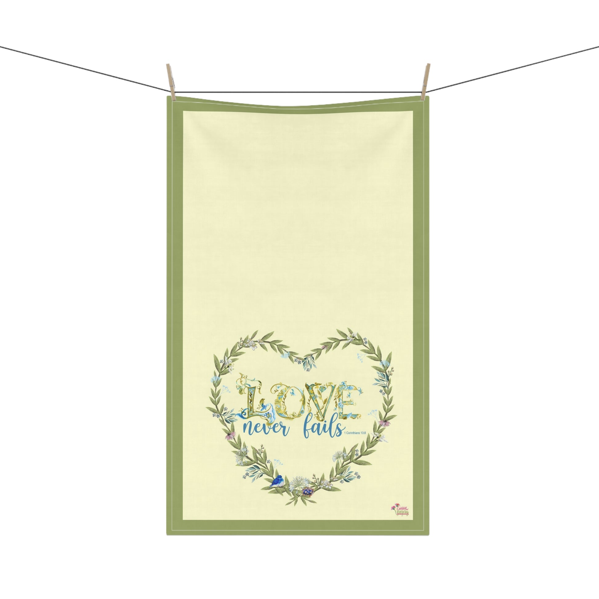Tea Towel with 'Love never fails' design on a green border, hanging on a line.