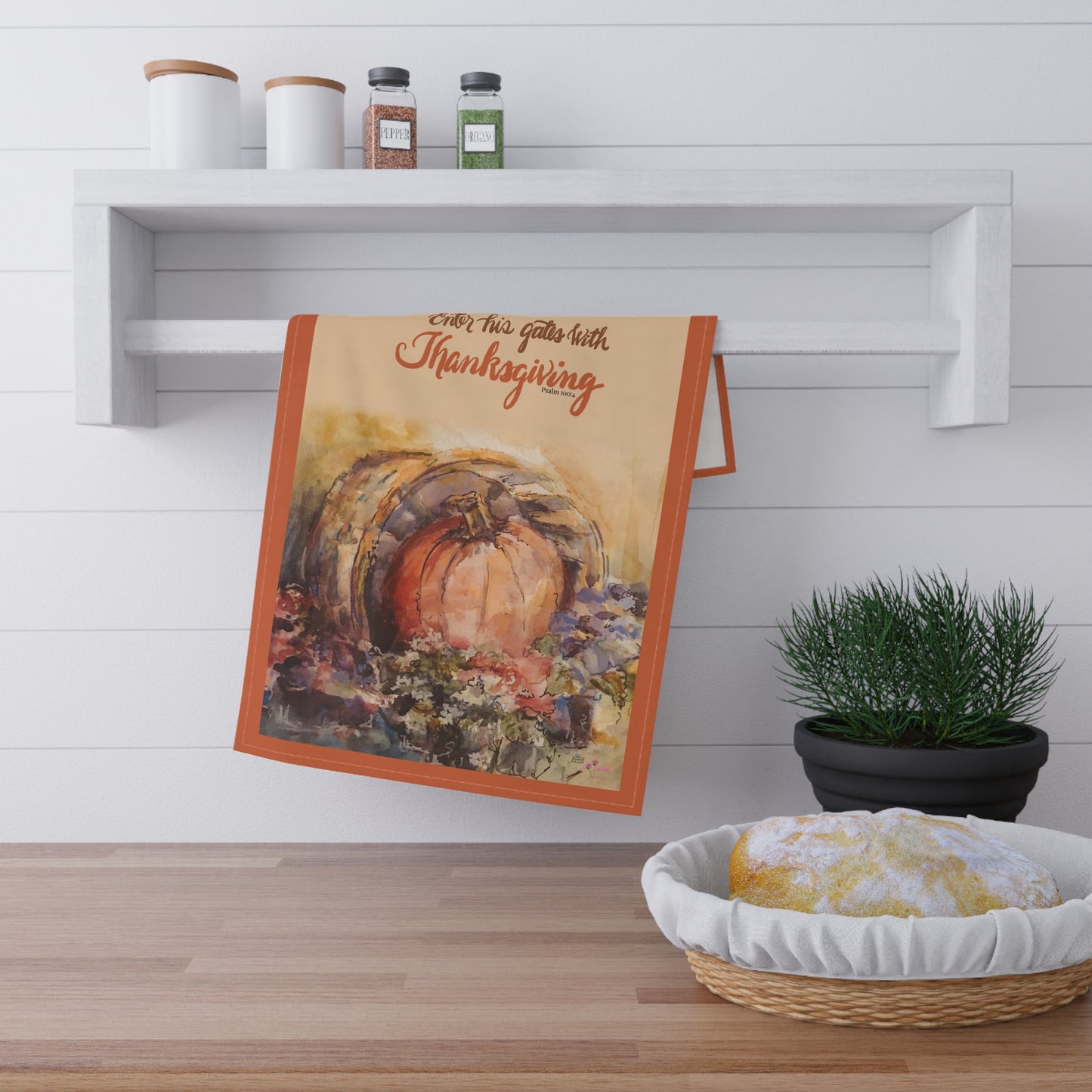 Decorative Thanksgiving kitchen towel with pumpkin design and Bible verse "Enter his gates with Thanksgiving" text on a wooden surface.