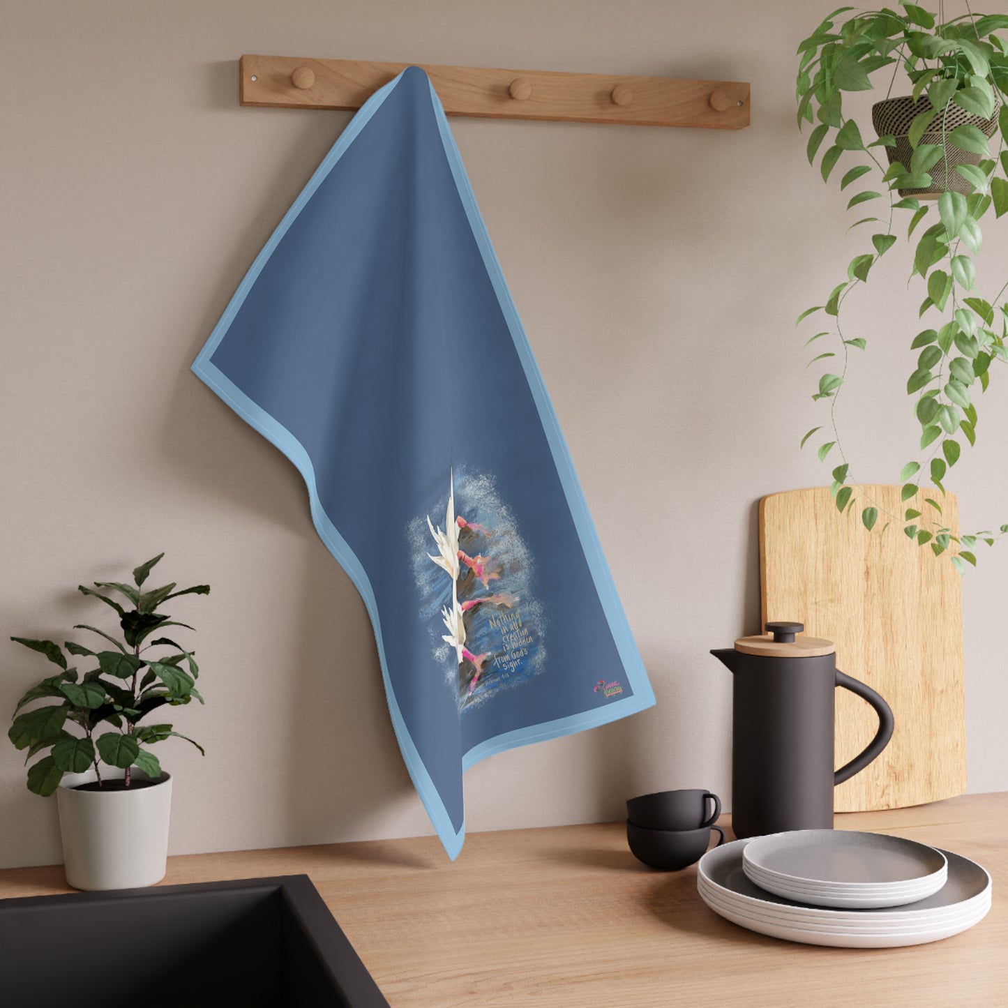 Blue kitchen tea towel with illustration of two ducks in pond hanging on a wooden rack in a kitchen setting.