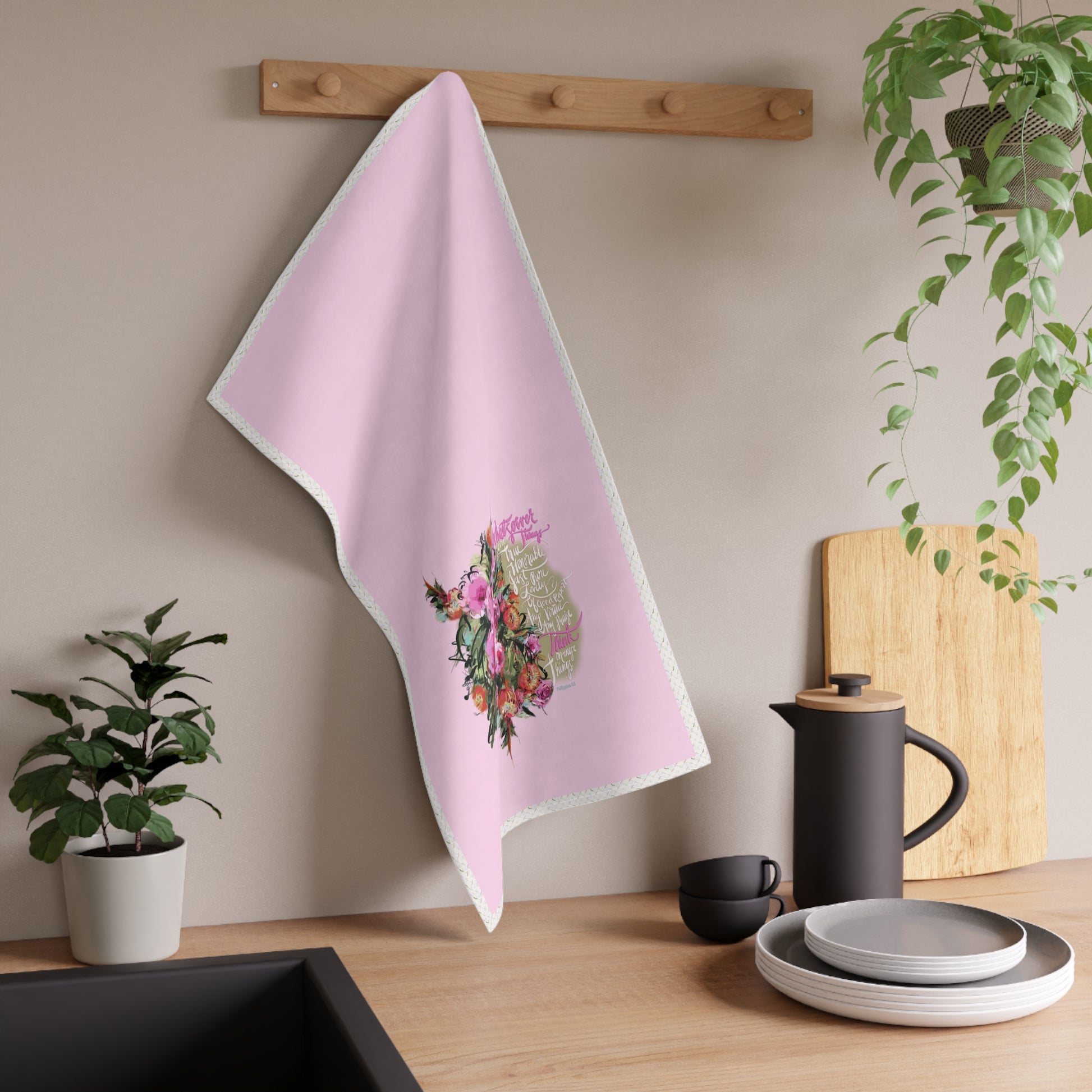 Pink tea towel with floral design hanging on a wooden rack in a kitchen setting.