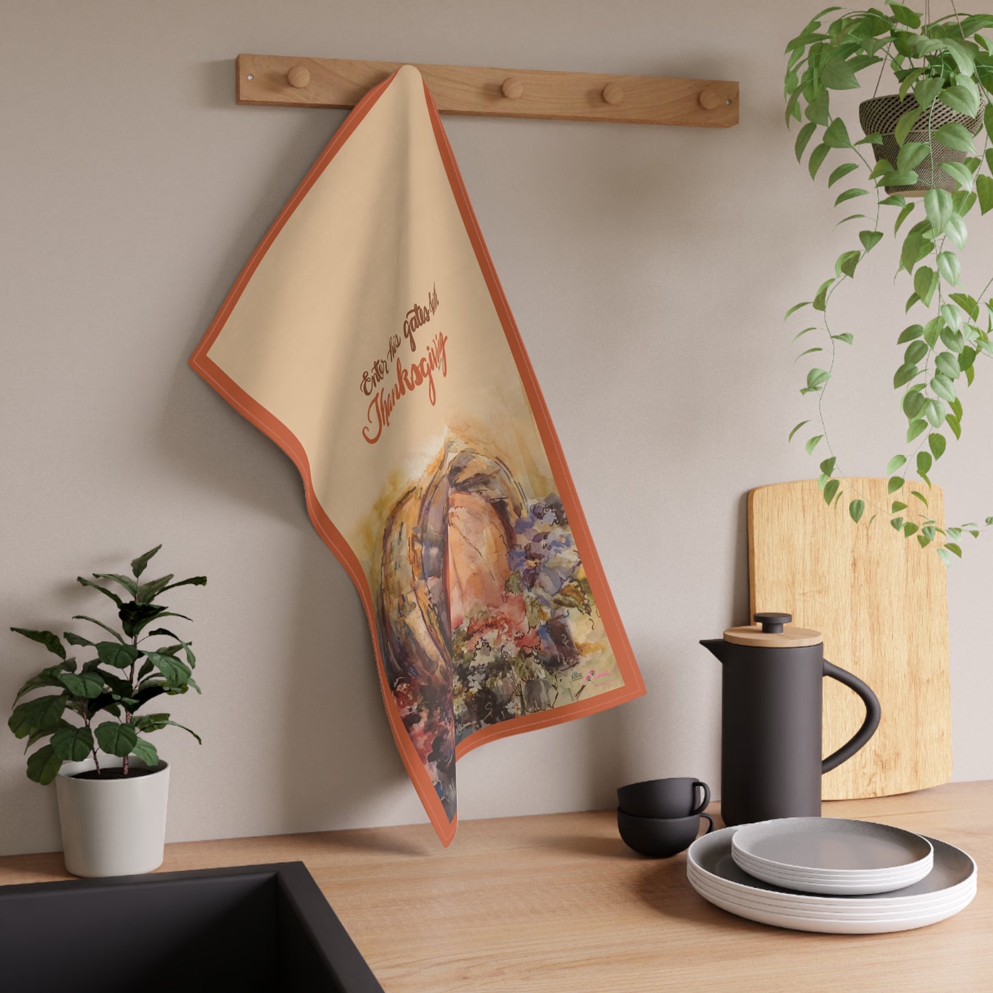 Decorative tea towel with pumpkin Thanksgiving design hanging on a wall above a kitchen counter.