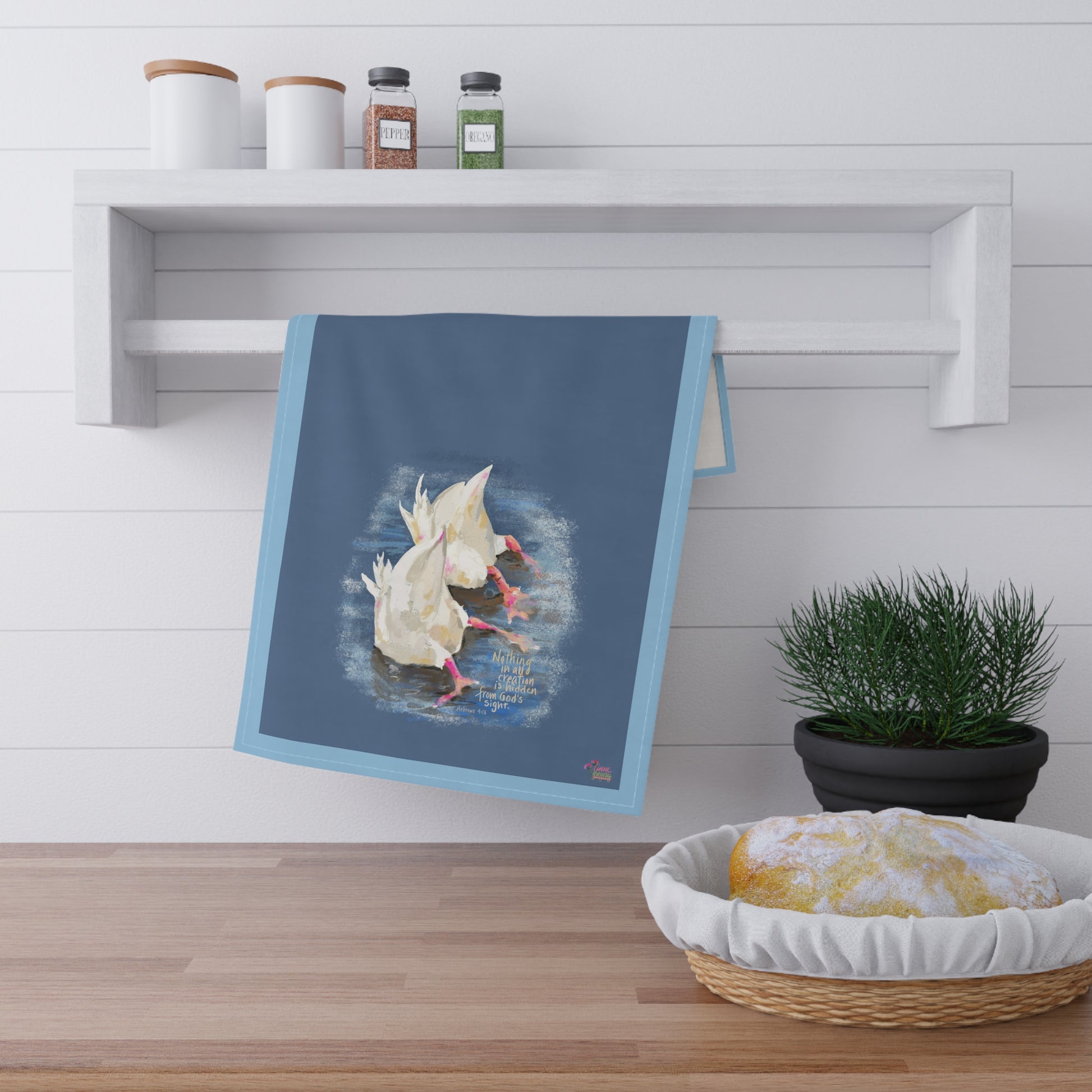 Kitchen towel with two ducks in water design and Bible verse "Nothing is hidden" hanging on a wooden shelf with kitchen items.