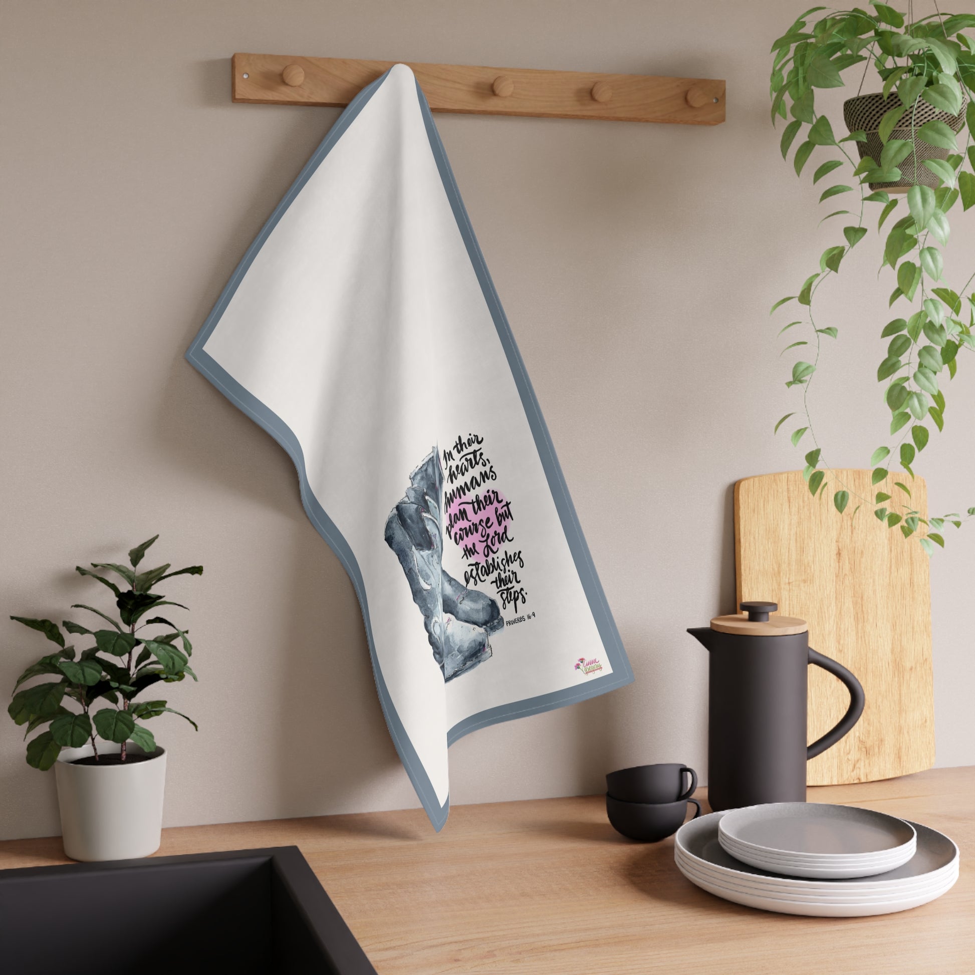 Kitchen towel with cowboy boot design hanging on a wooden rack, surrounded by kitchen items and plants.