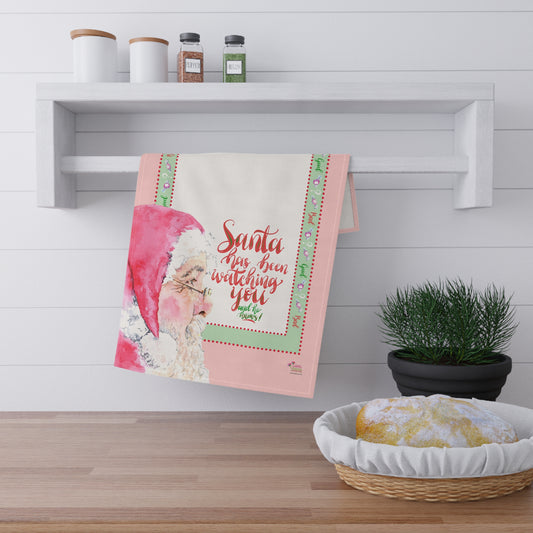 Decorative tea towel with Santa Christmas design hanging on a wall shelf above a kitchen counter.