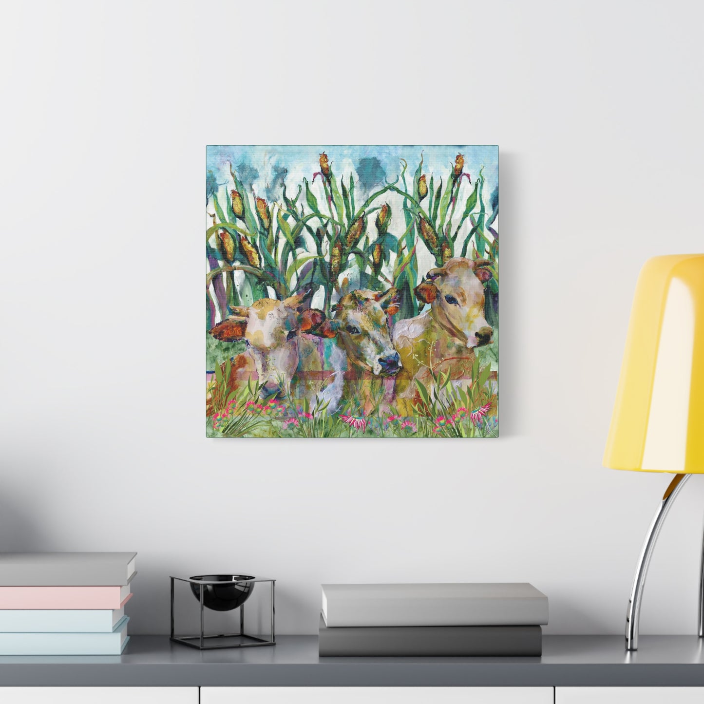 Canvas print of cows in a field with corn on a wall above a desk.
