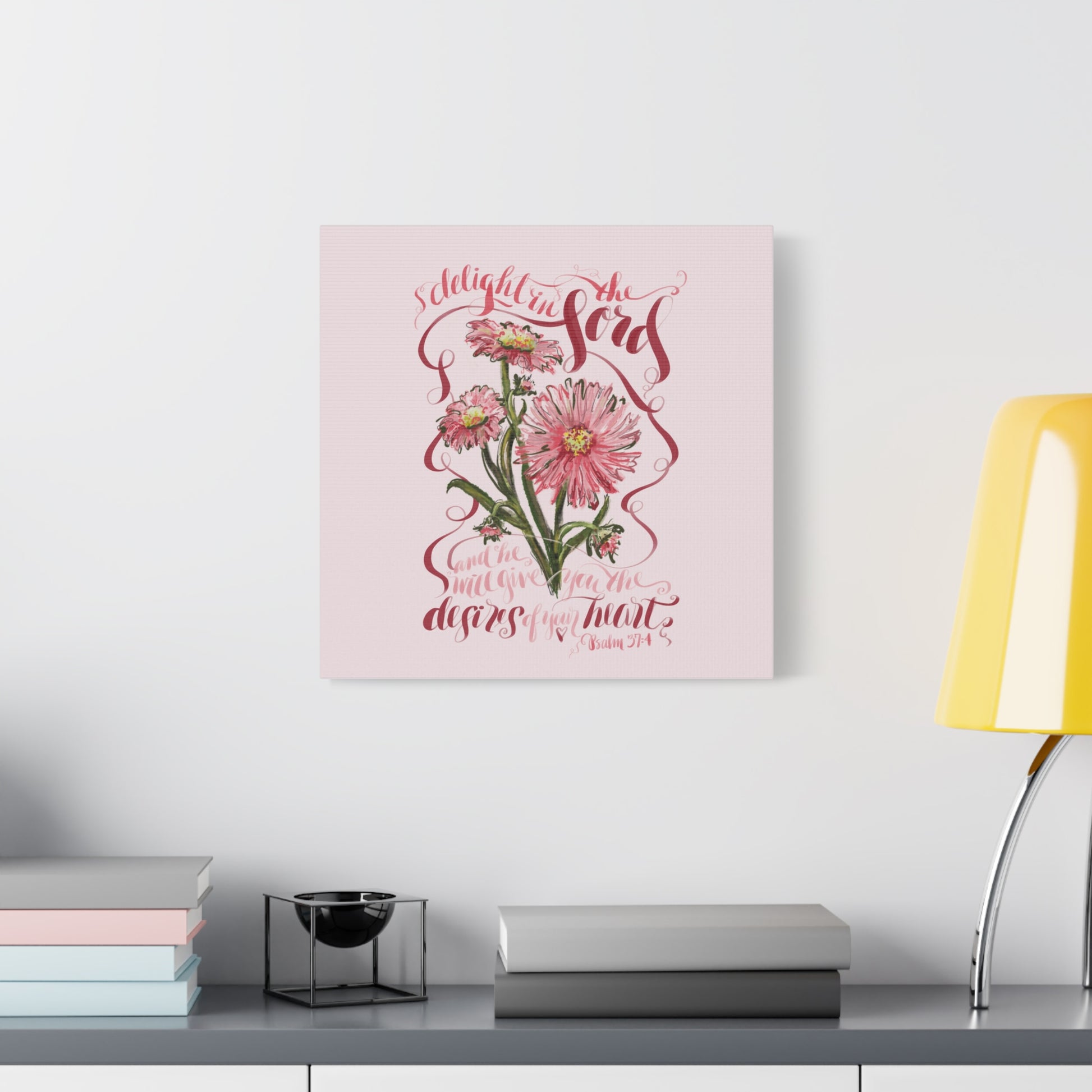 Decorative wall art with floral design and calligraphy Bible Verse Delight in the Lord and he will give you the desires of your hear;  on a pink background, placed on a shelf.