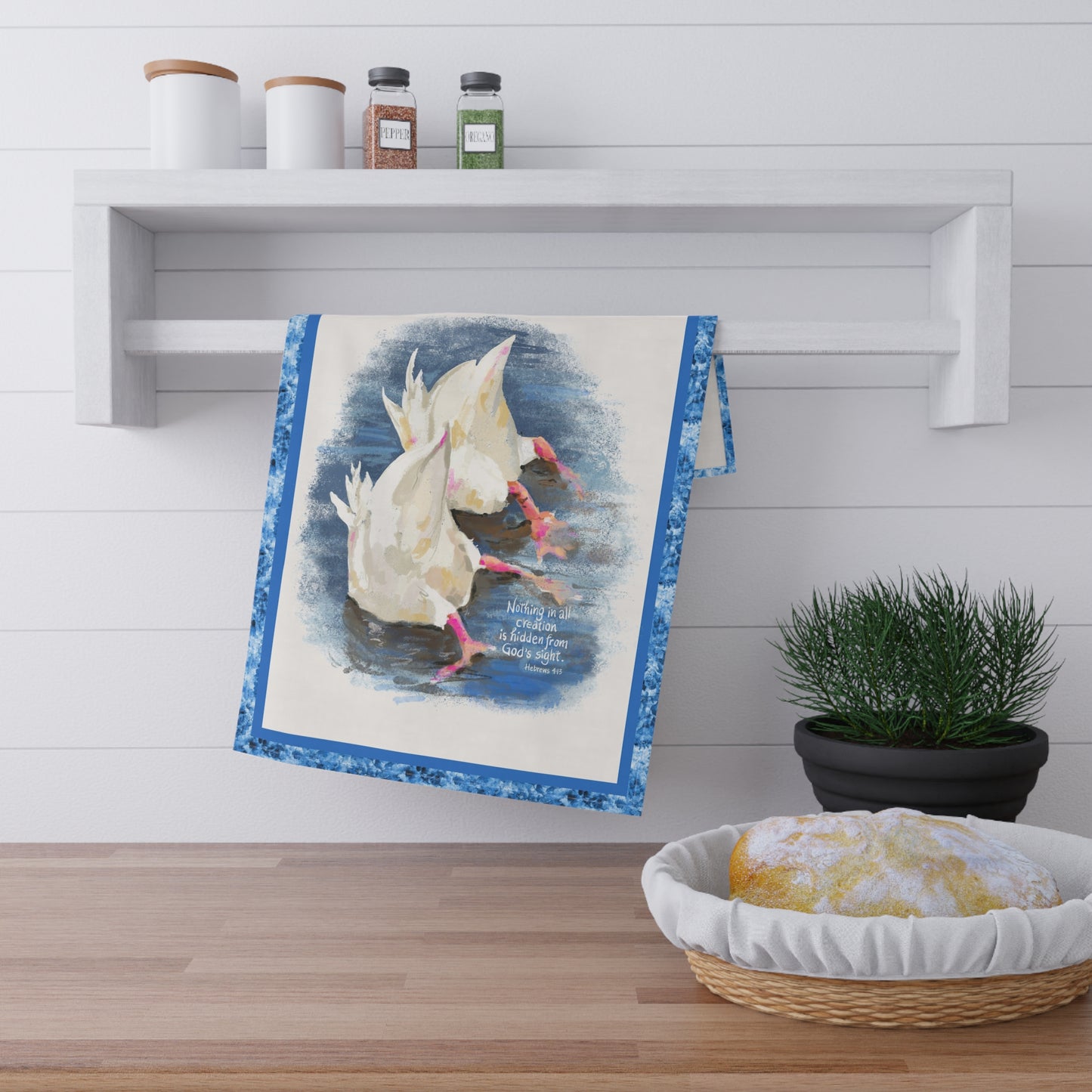 Decorative towel with a duck in water design and Bible Verse, Nothing in all creation is hidden in God's sight; hanging on a wall above a wooden shelf with a plant and bread basket.