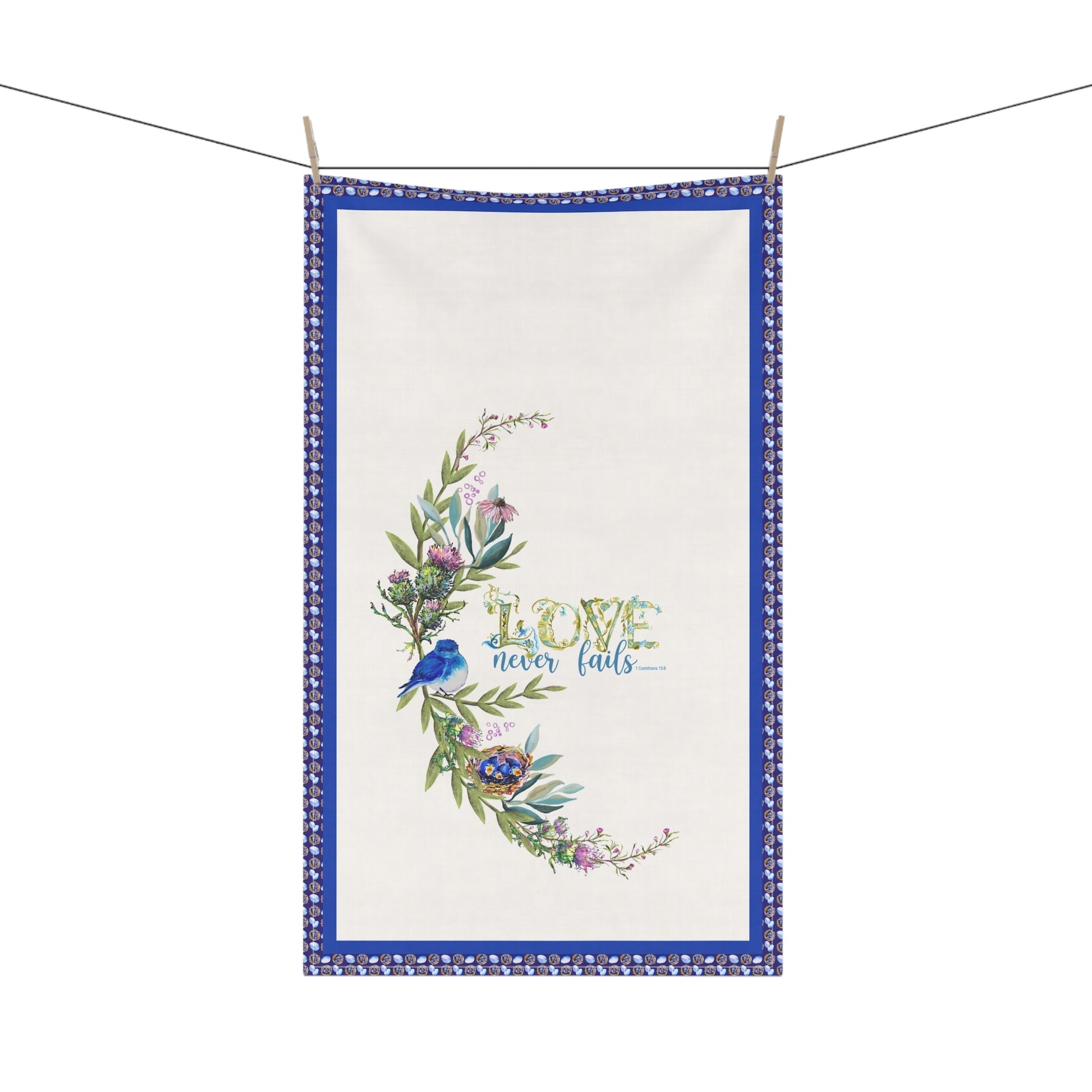 Decorative tea towel with floral design and 'Love never fails' text, hanging on a line.