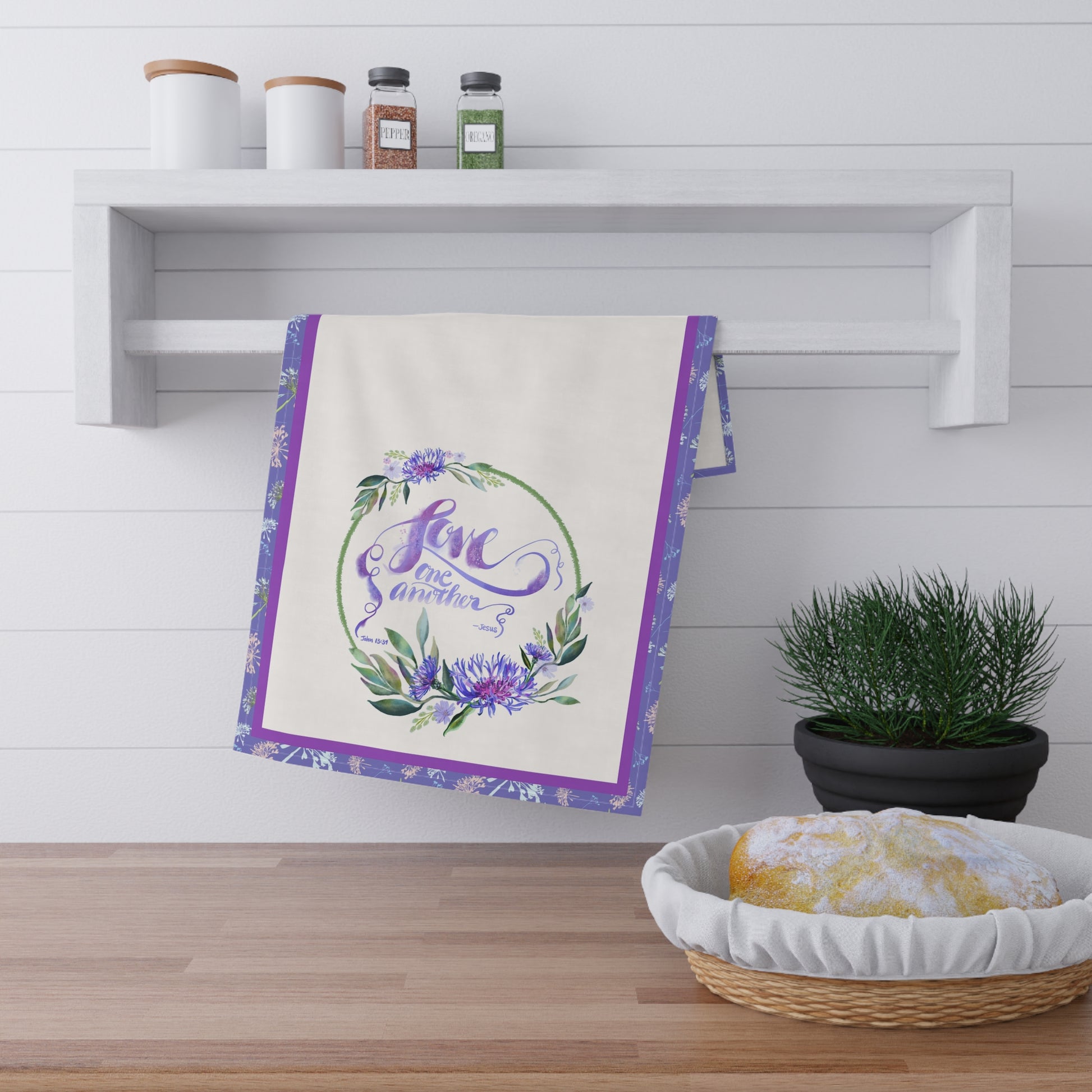 Decorative tea towel with floral design and Bible Verse Love one another on a kitchen counter.